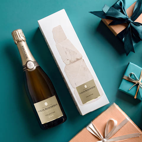 Eine Flasche Louis Roederer Sekt steht neben einer geschmackvoll gestalteten Verpackung. Um sie herum liegen hübsch verpackte Geschenke mit unterschiedlichen Bändern auf einem blauen Untergrund.
