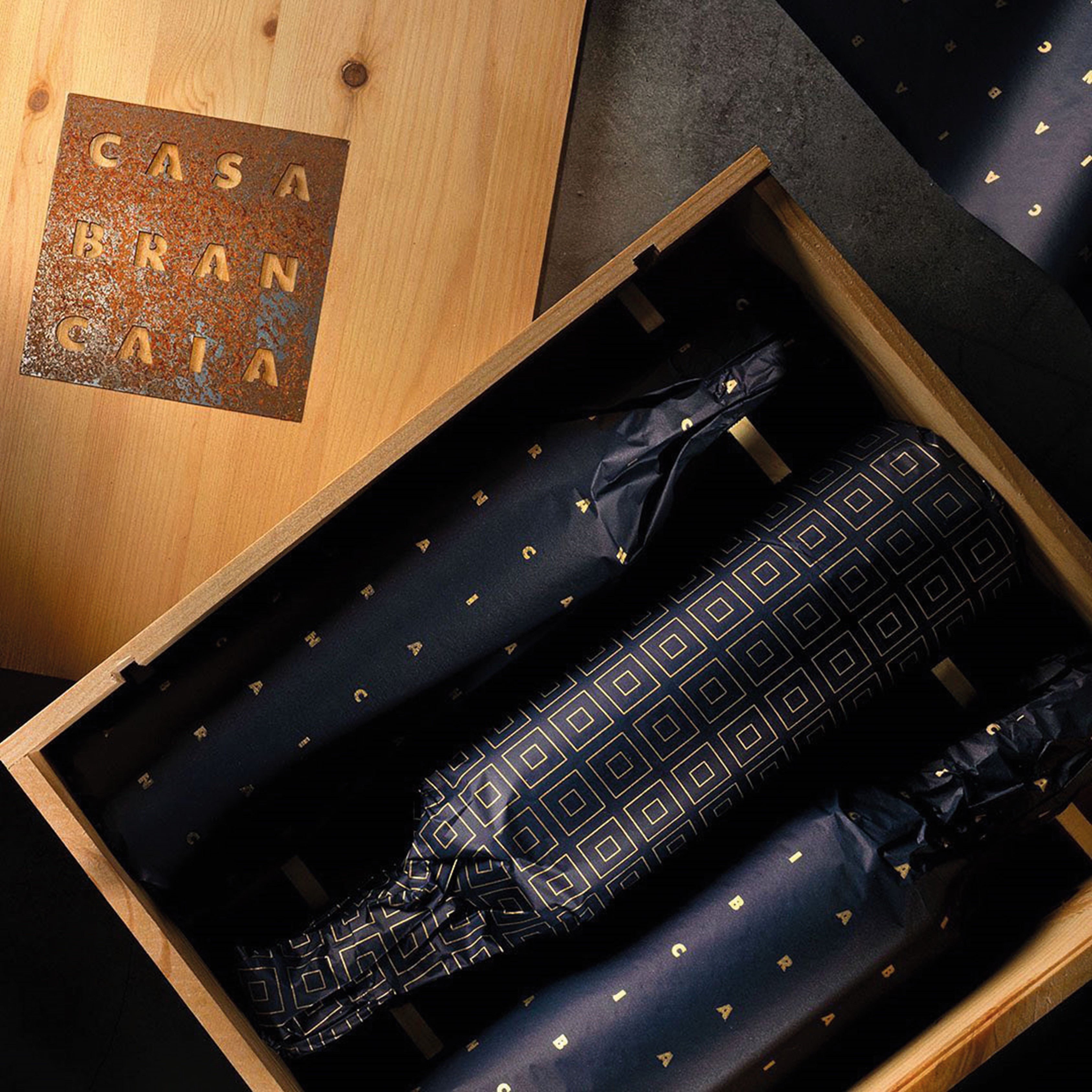 Holzkiste mit dem Aufdruck -CASA BRANCA-. Darin liegen drei in schwarzes Papier mit goldener Schrift eingewickelte Flaschen. Die Kiste hat einen rustikalen, eleganten Charme.