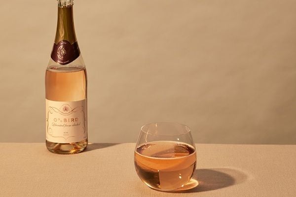 Eine Flasche Roséwein steht auf einem Tisch, neben einem Glas, das ebenfalls mit Rosé gefüllt ist. Der Hintergrund ist in neutralen Farben gehalten.