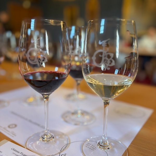 Drei Weingläser stehen auf einem Tisch, zwei mit rotem Wein und ein Glas mit weißem Wein. Im Hintergrund sind verschwommene Menschen und eine angenehme Umgebung zu erkennen.